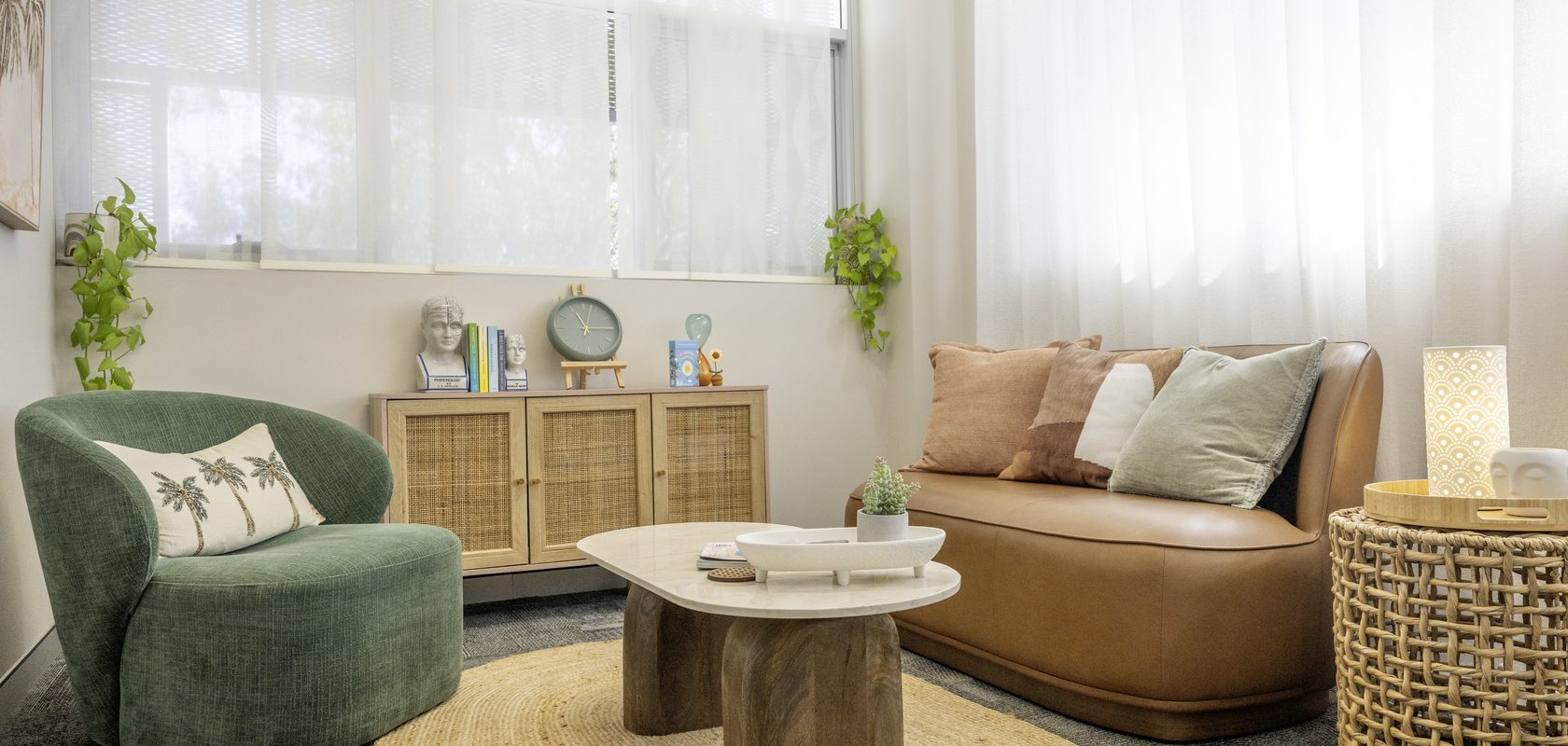 A consulting room with a tan leather sofa, green armchair and jute rug