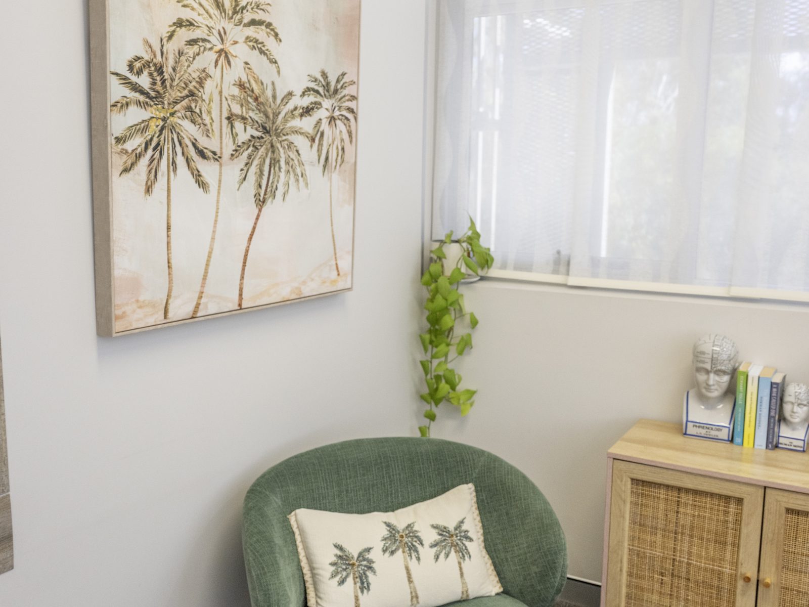 A green armchair in a corner beneath palm artwork