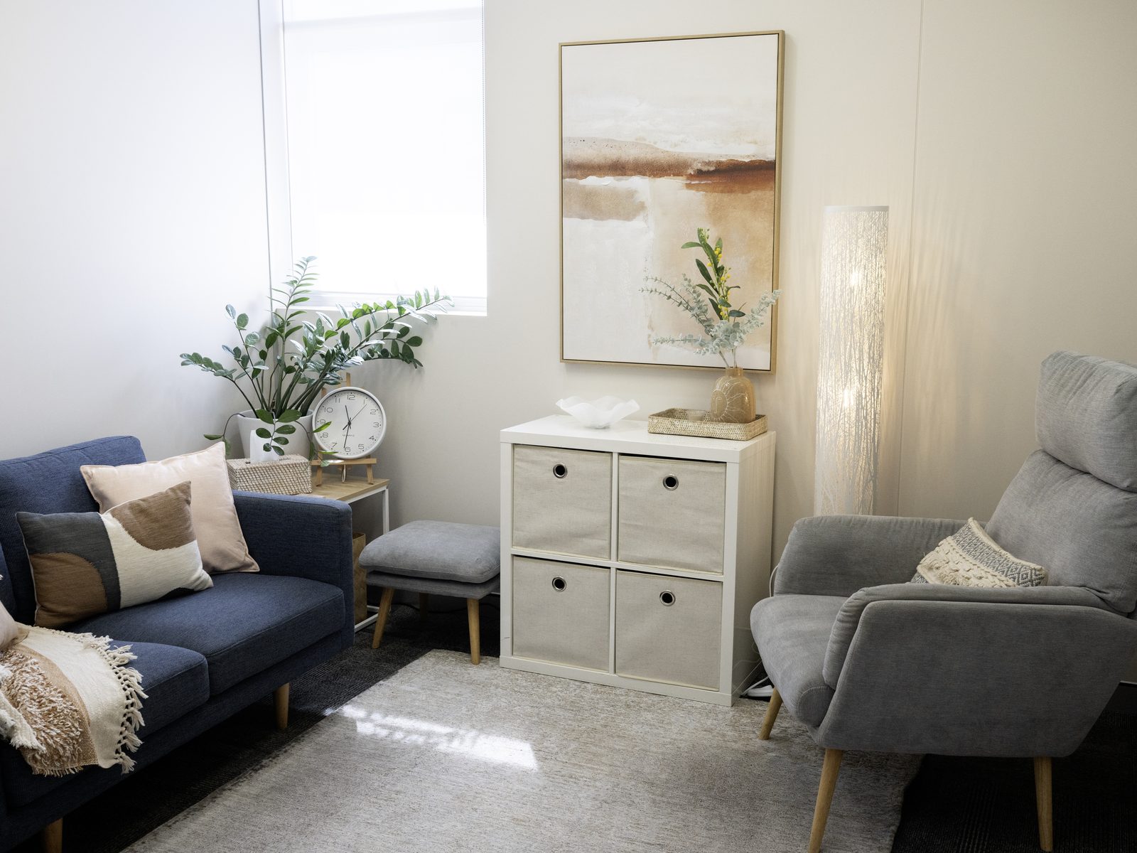 A consulting room with a navy sofa, grey armchair and soft abstract artwork