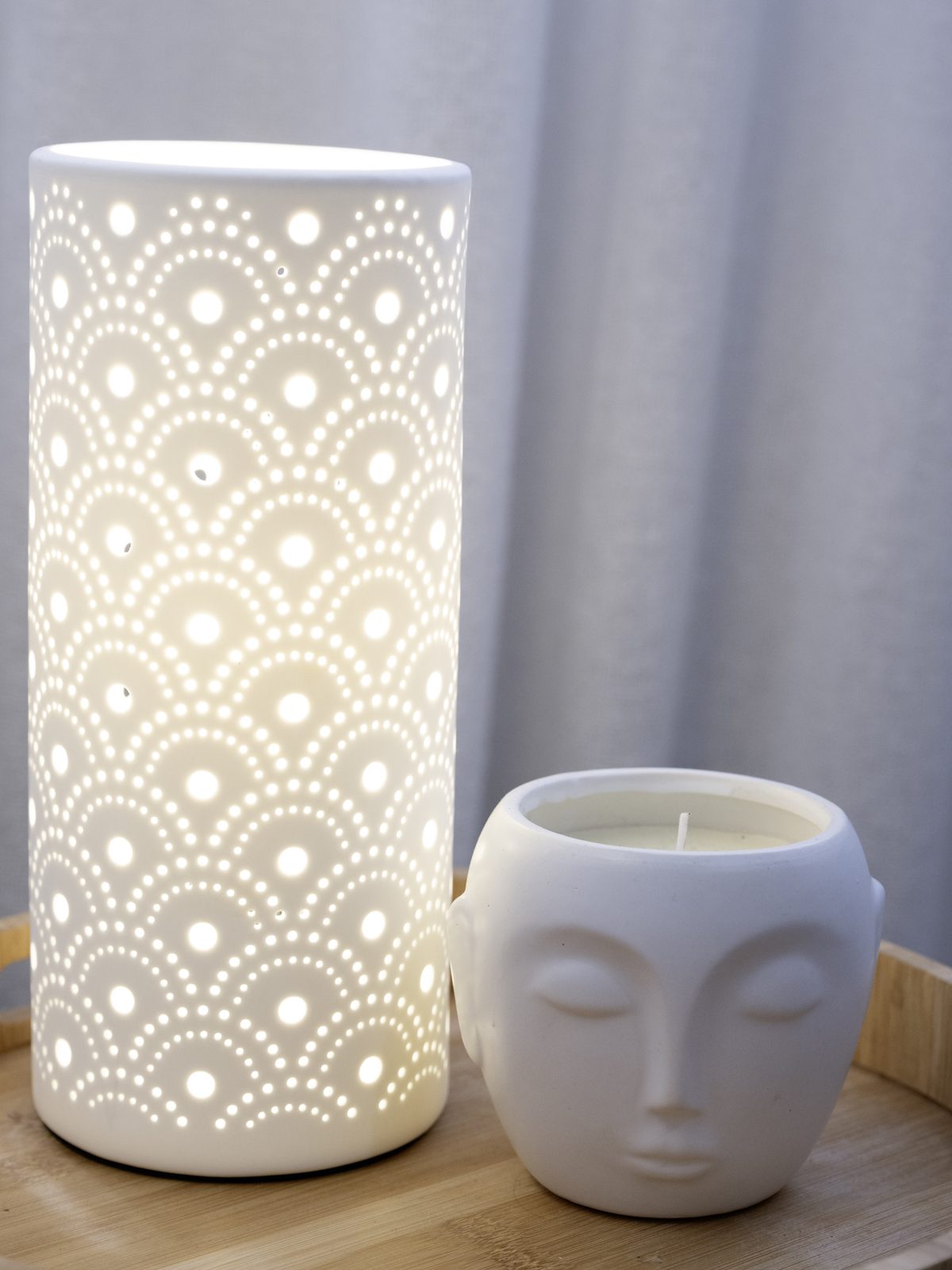 A pierced ceramic lamp glowing beside a white face-shaped candle pot