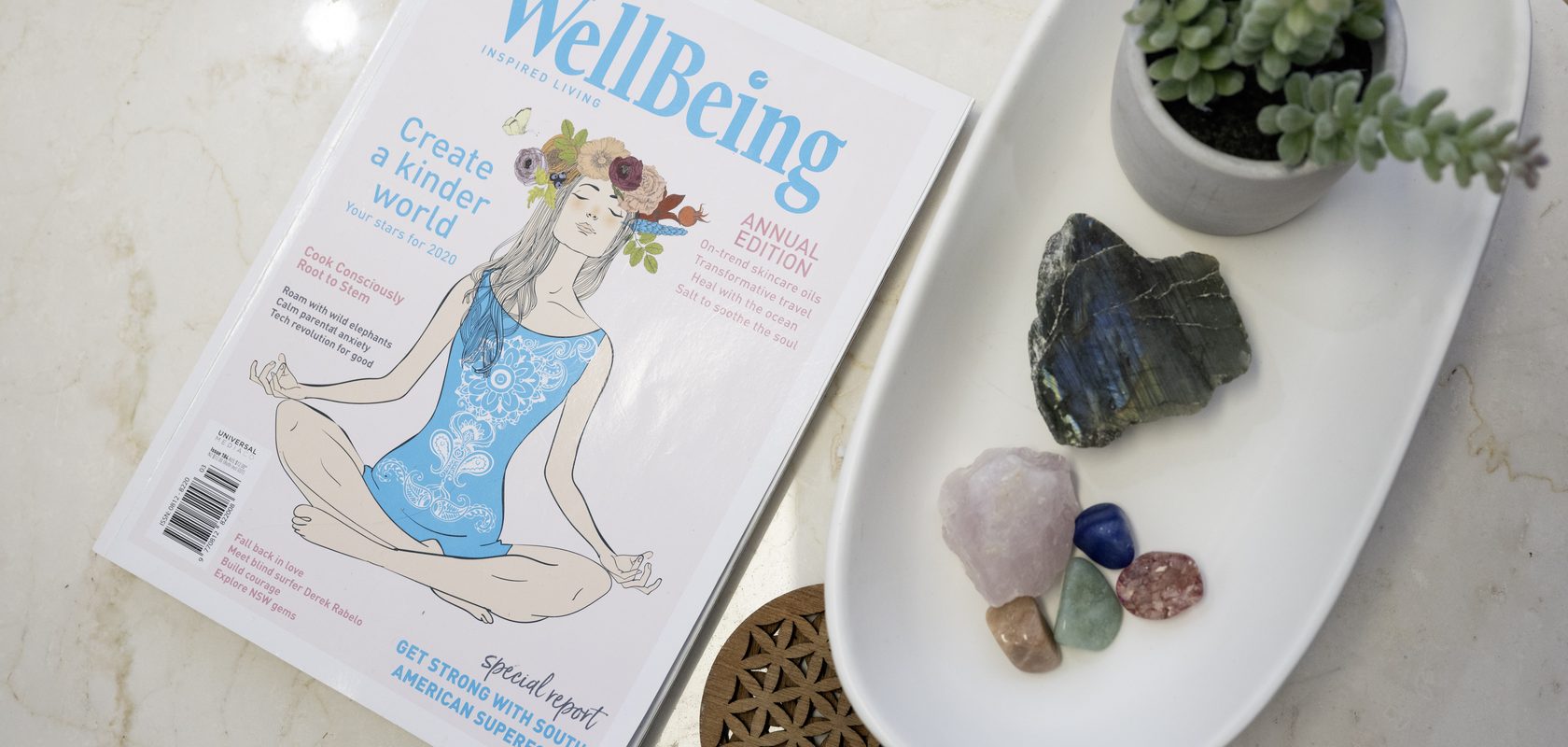 A wellbeing magazine beside a dish of crystals and a small succulent on a marble bench