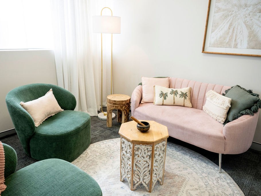 Two green armchairs and a blush pink sofa around a carved timber table with a singing bowl